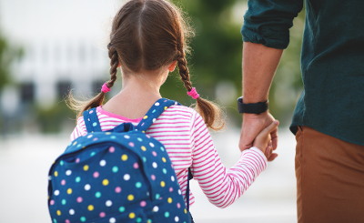 Girl walking to school Photograph from behind of a young girl wearing a backpack and holding her father/male carer's hand