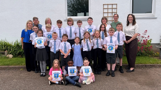 Photograph of group of school pupils from Our Lady's RC Primary School and their teachers standing in a group outside the school building holding its of paper saying 'Very Good'